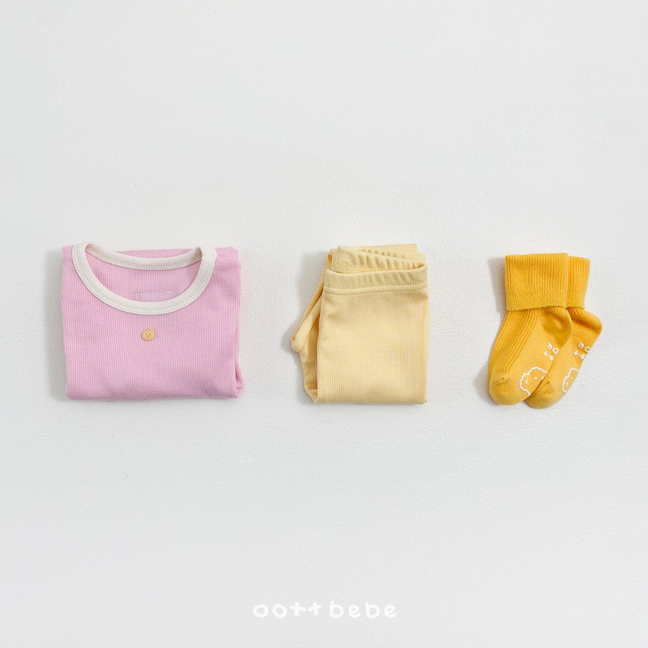 摺疊好的粉色上衣與黃色褲子，旁有黃色襪子，展示坑條棉材質細節。