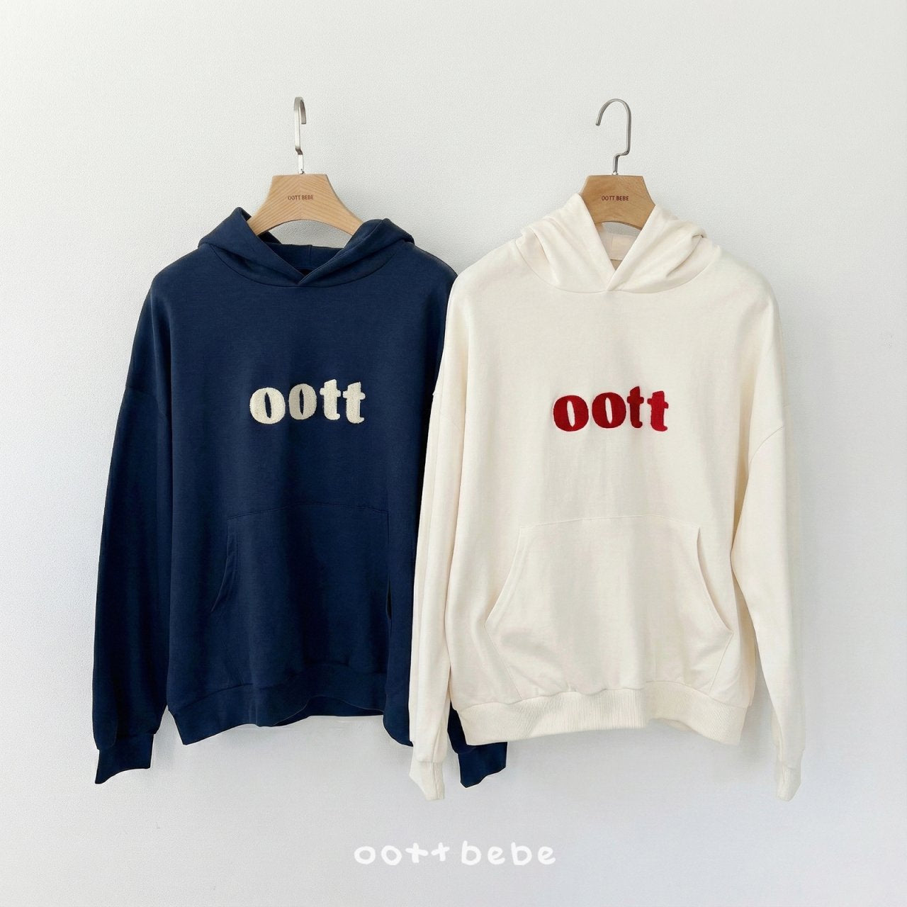 兩件大人款 oottbebe 連帽衛衣掛拍展示，左為海軍藍，右為奶油白，展示寬鬆版型。