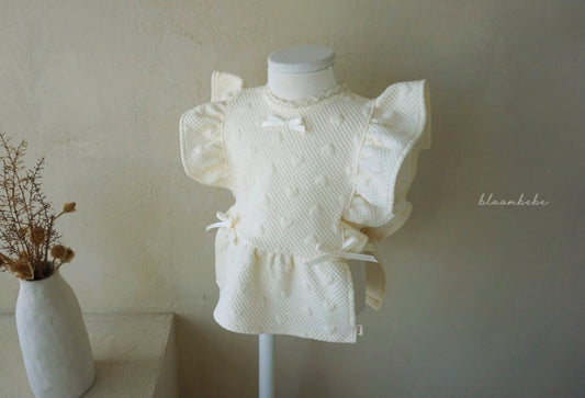 韓國童裝 bloombebe 奶油色背心正面展示，具備寬版荷葉飛袖、蕾絲領口滾邊與胸前可愛蝴蝶結設計。