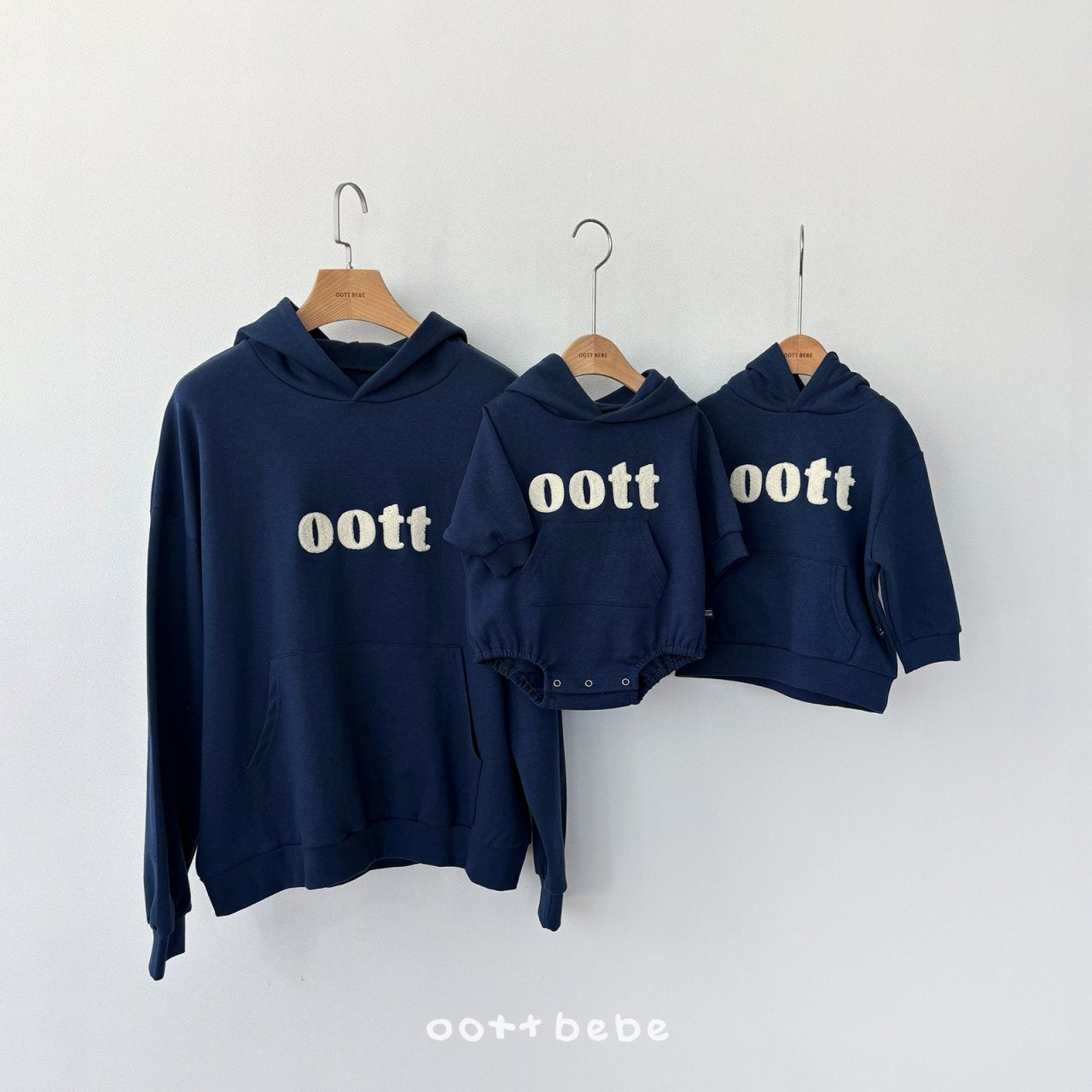 oottbebe 海軍藍系列親子裝平拍，左起為大人款帽T、中間為嬰兒連帽包屁衣、右邊為兒童款帽T，皆有米白色立體Logo。