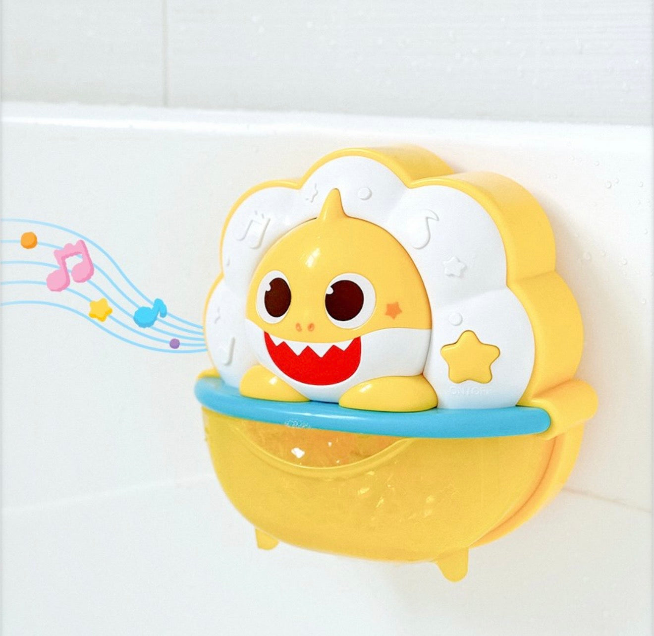 Baby Shark 泡泡玩具掛在白色浴室牆上的側面特寫，圖示畫有音符從玩具飄出，代表玩具正在播放音樂。