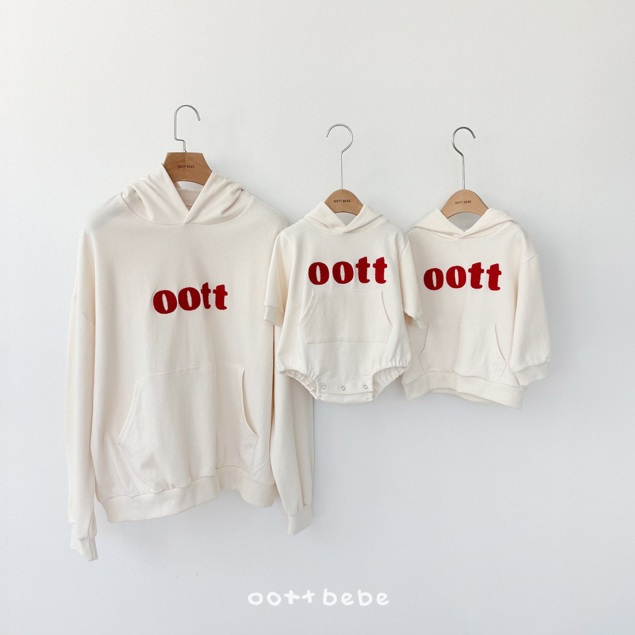oottbebe 奶油白系列親子裝平拍，左起為大人款帽T、中間為嬰兒連帽包屁衣、右邊為兒童款帽T，皆有紅色立體Logo。